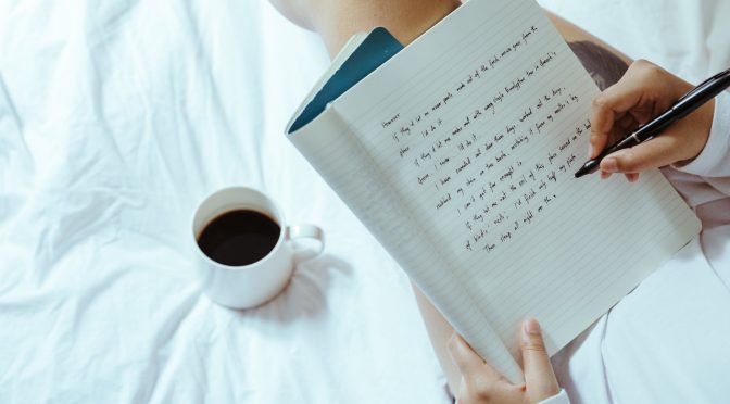 crop woman with coffee writing in notebook on bed
